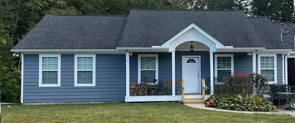 Blue suburban house with white trim, green lawn, and contact number for real estate.