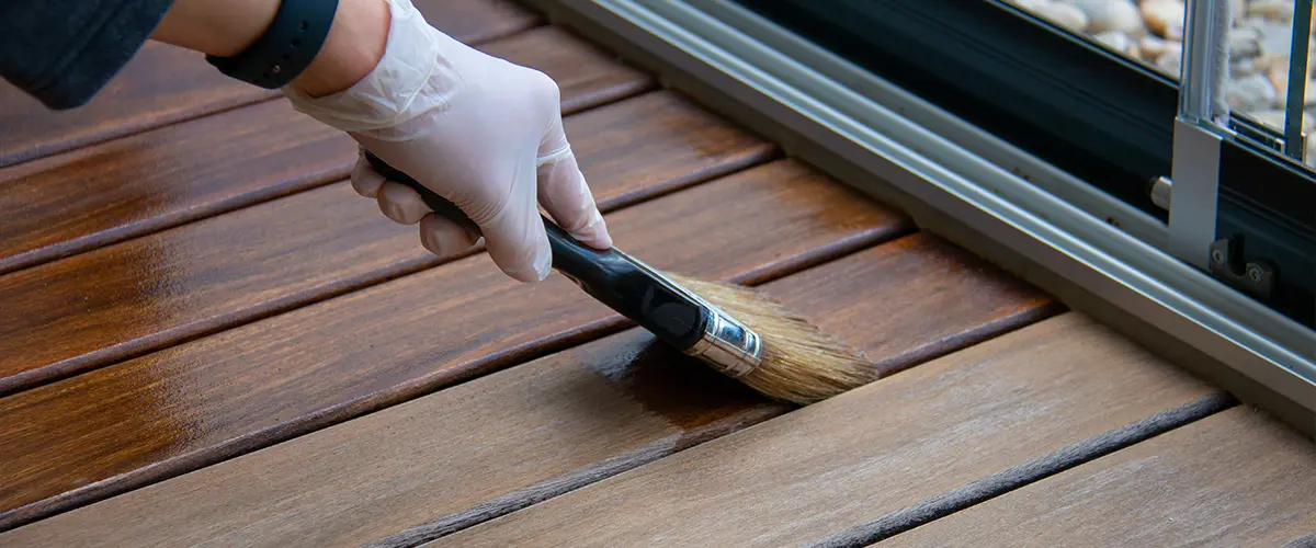 Deck staining, worker applying deck oil on decking boards with paint brush, hardwood terrace renovation