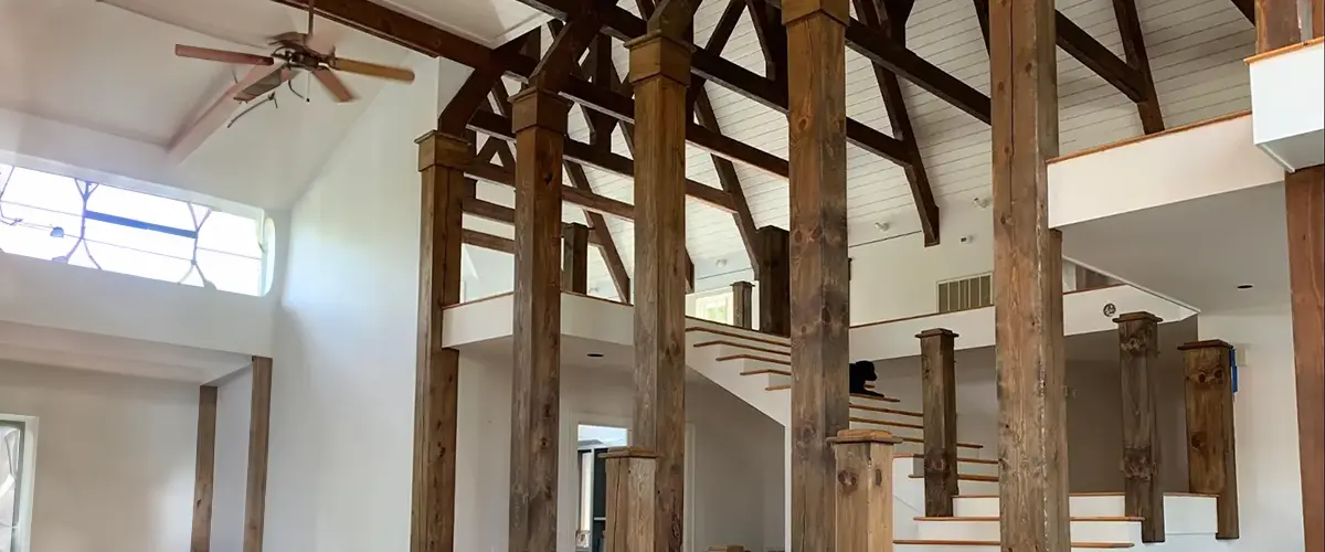 Spacious rustic interior with exposed wooden beams, modern staircase, and high ceilings, perfect for barn-style home renovation ideas.