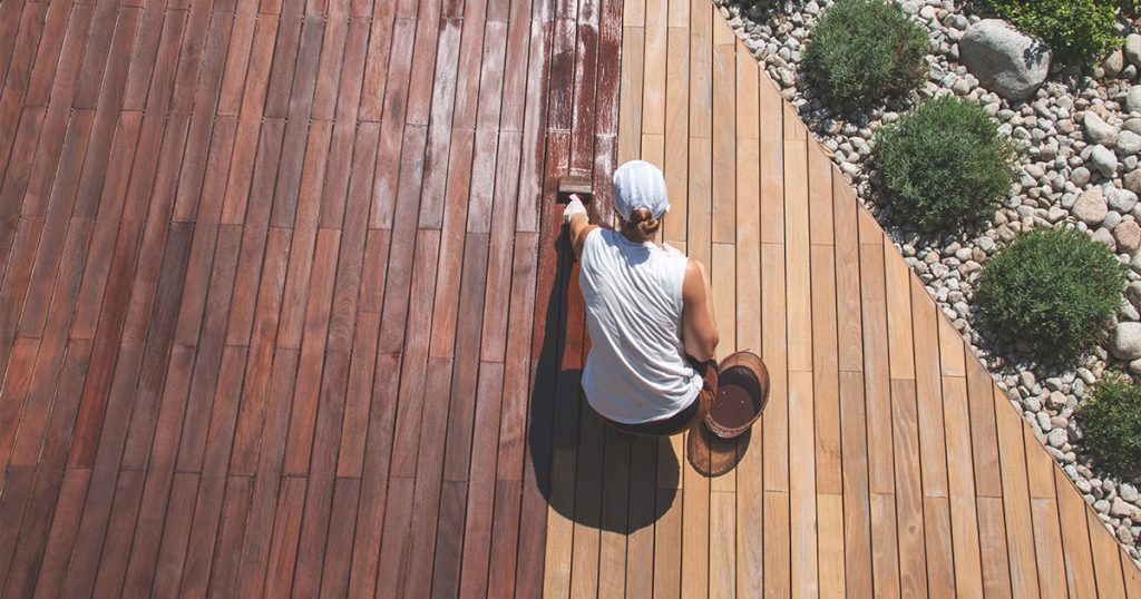 Wood deck renovation treatment, the person applying protective wood stain with a brush, overhead view of ipe hardwood decking restoration process