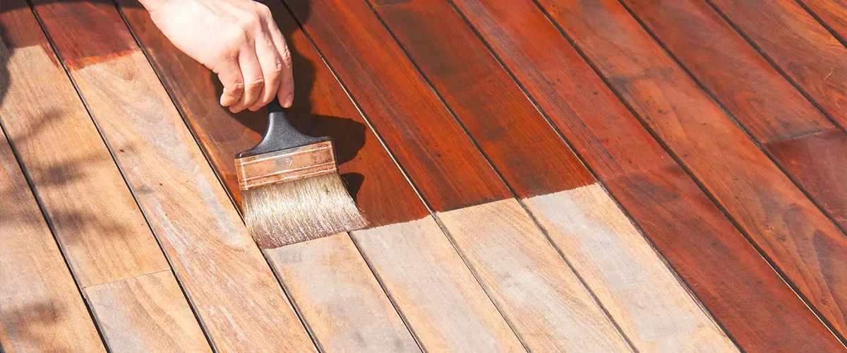 Worker staining an ipe wood deck with a paintbrush, highlighting outdoor deck maintenance and refinishing techniques for durability.