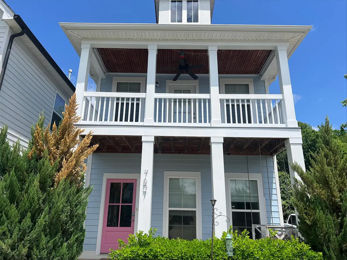 a light blue and white house with a balcony and a pink door