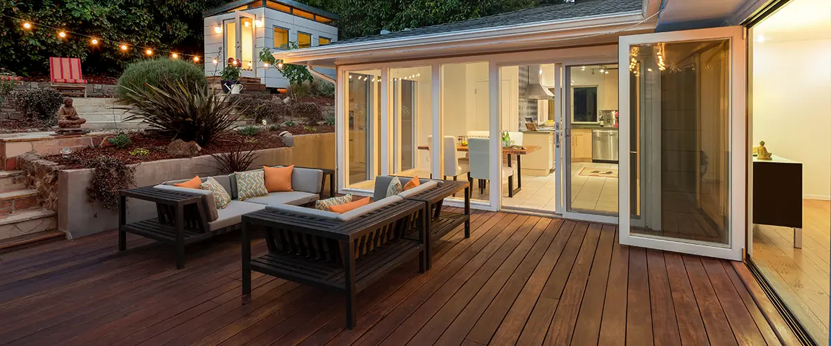 Modern wooden deck in Franklin, with outdoor seating, string lights, and garden landscaping, connected to a house with large sliding doors.