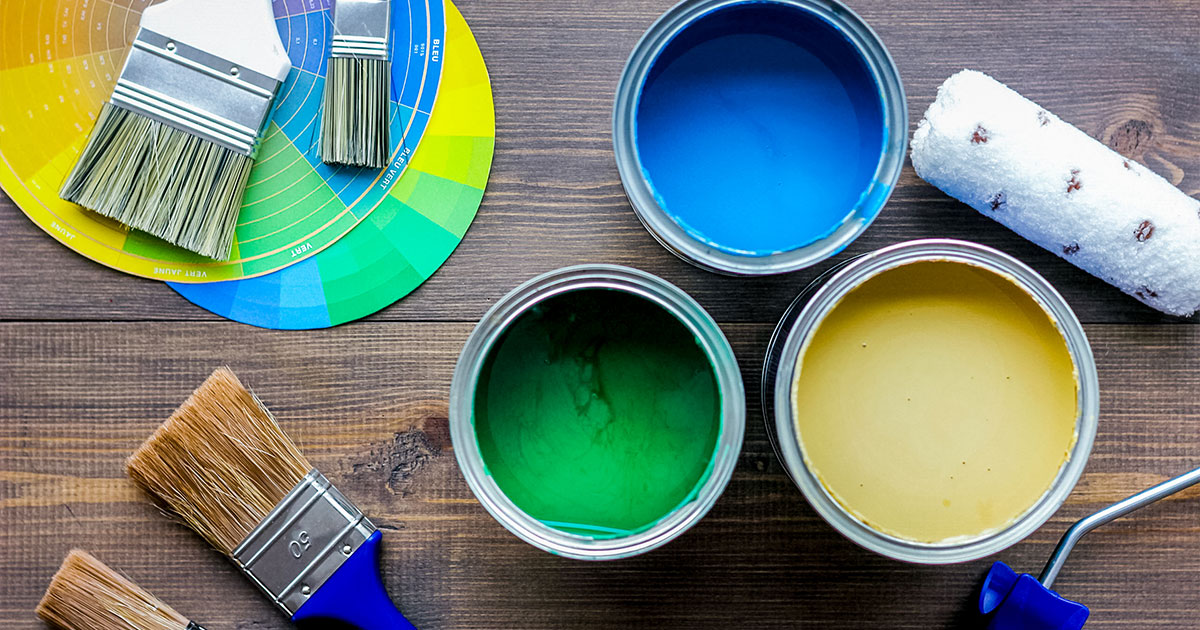 Open paint cans in blue, green, and yellow with brushes and color wheel for choosing the right shade. Oil vs Latex Exterior Paint