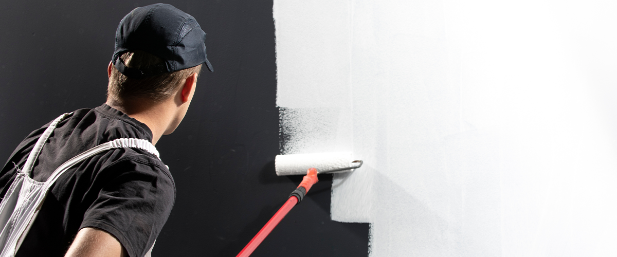 Painter applying white paint over a black wall with a roller.