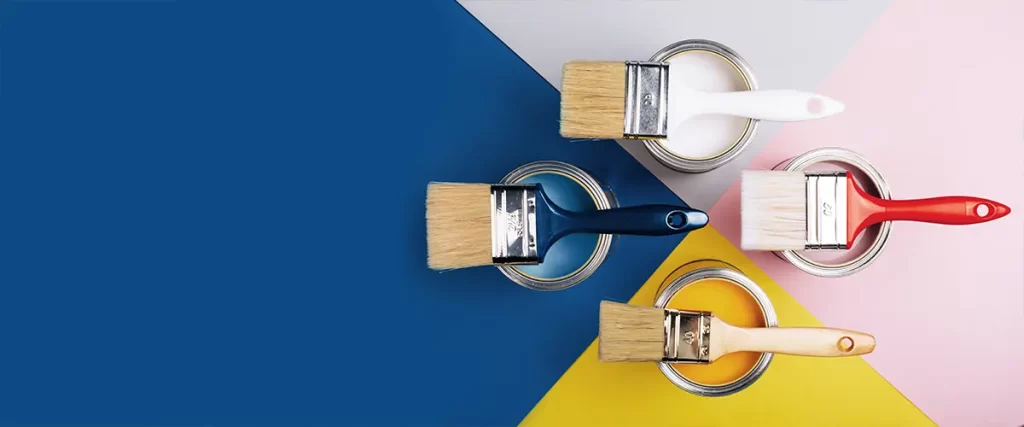 Four paintbrushes resting on open paint cans with blue, white, and yellow backgrounds, showcasing color selection for painting.