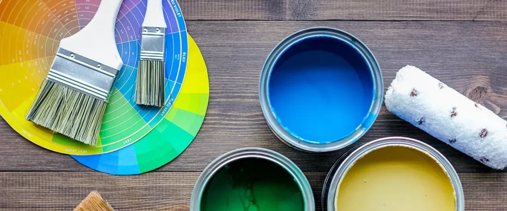 Open paint cans with brushes and a color wheel on wood surface
