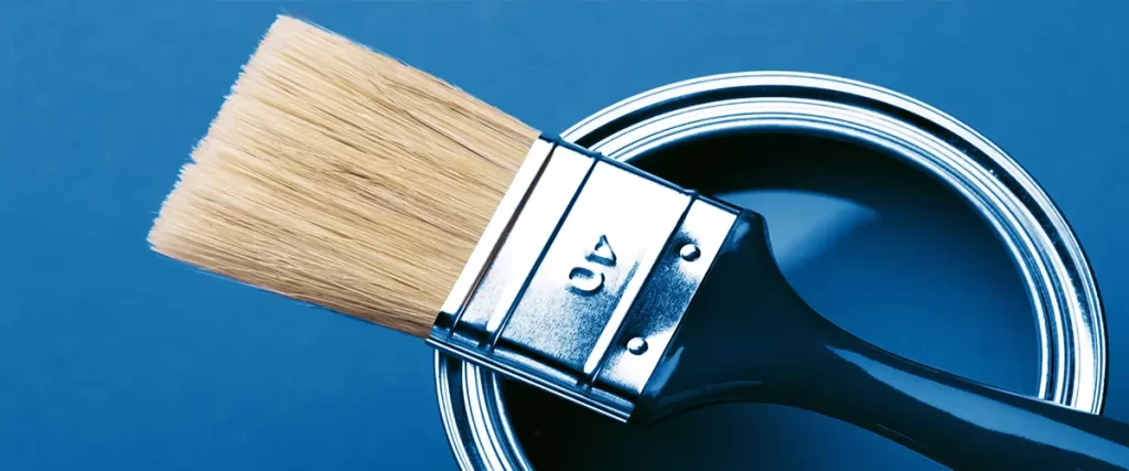 Paintbrush resting on can of blue paint against blue background