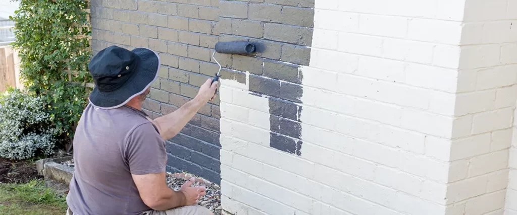 man painting exterior brick wall with dark paint