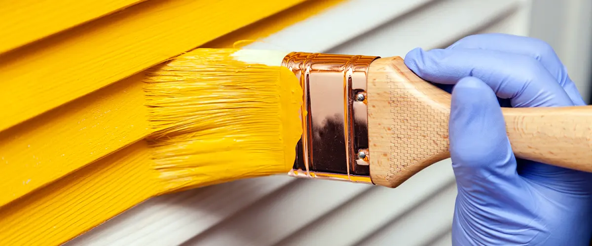 Close-up of yellow paint being applied to siding