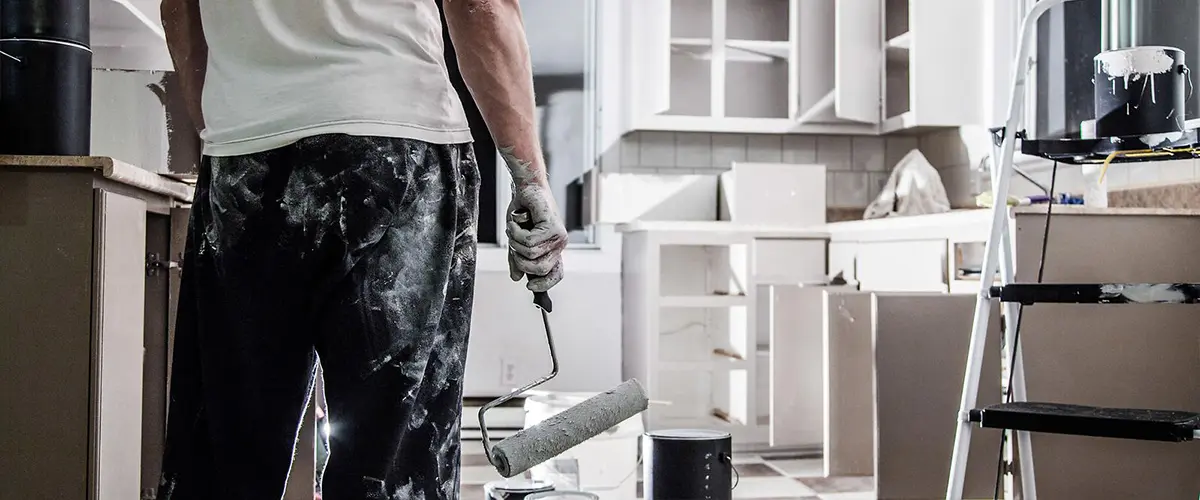 Painter holding roller in kitchen with cabinet doors removed