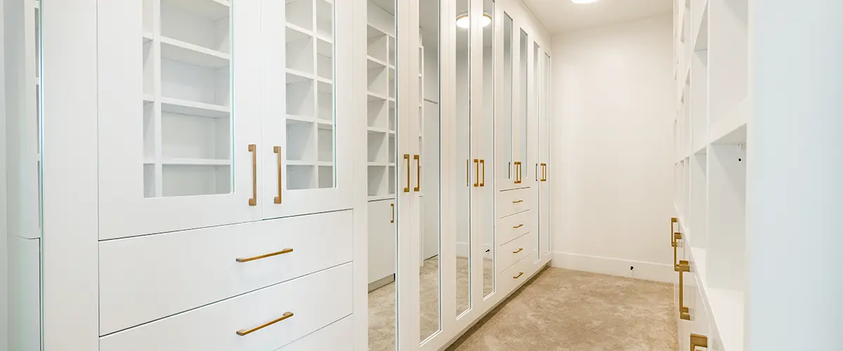 White walk-in closet with glass cabinet doors and gold handles
