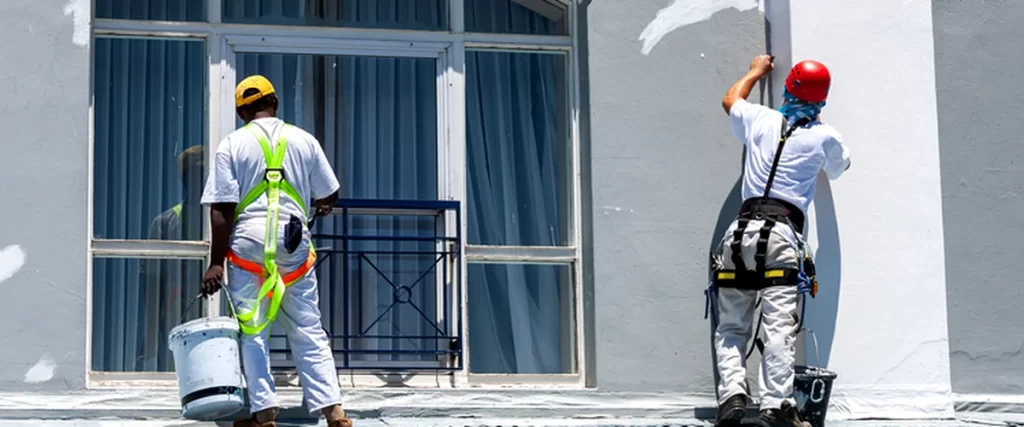 commercial painting professional contractors applying white paint to commercial building exterior wall
