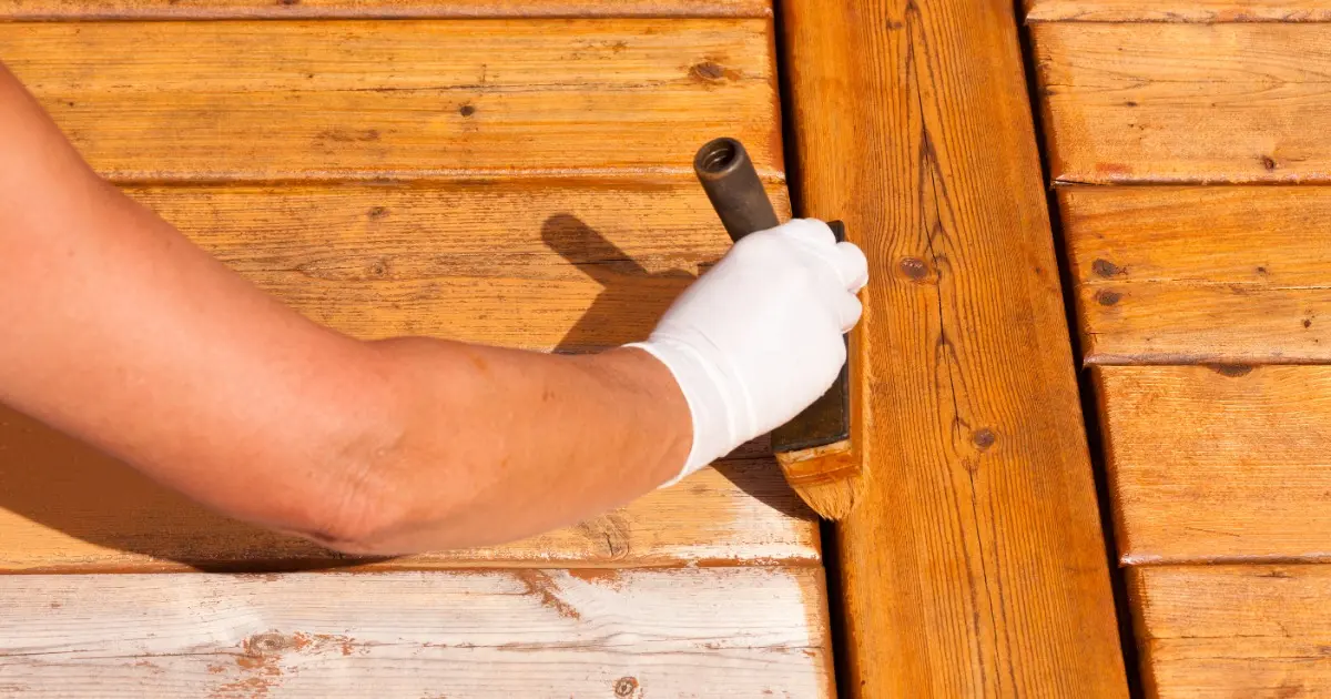 A person in white gloves staining a wooden deck