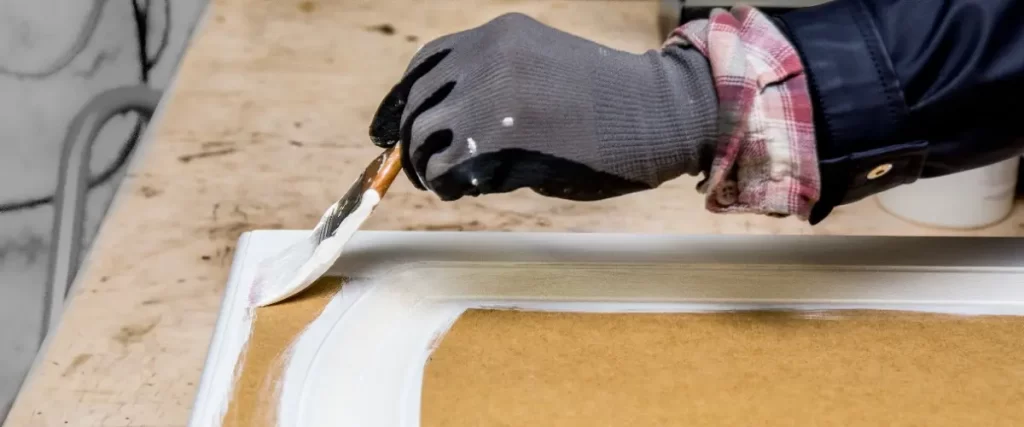 A person paints a wooden piece with a brush, focusing on the surface and applying a fresh coat of color