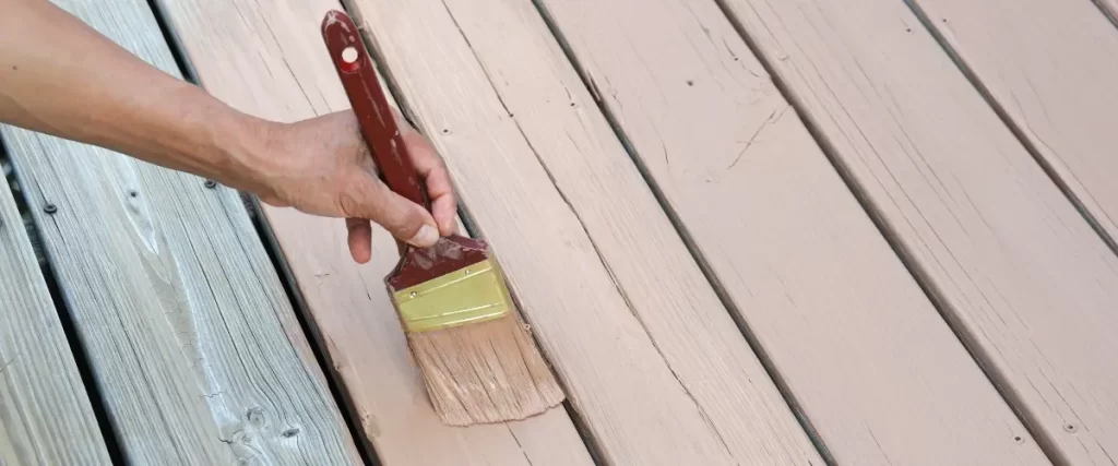 A person staining a wooden deck with a brush, focused on applying a fresh coat of paint