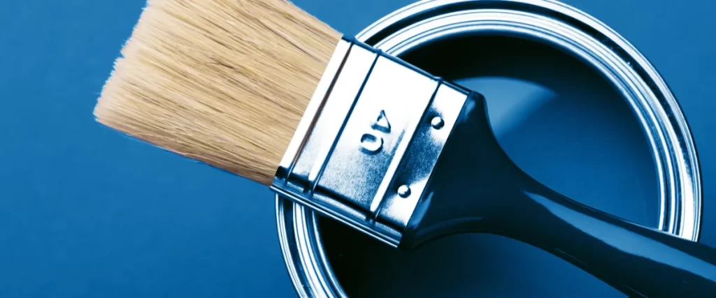 a paint brush resting on the rim of an open can of blue paint