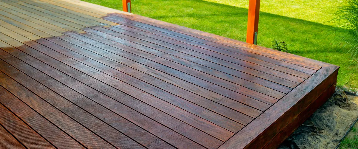 An elevated wide shot of a large outdoor wooden deck showing the contrast between the original light wood and a freshly finished section with dark brown staining.