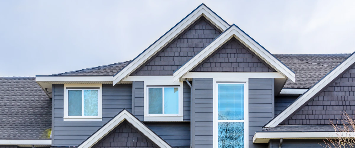 Close up view of a modern two-story home featuring clean grey siding, dark shingles, and crisp white trim highlights protected by high-quality exterior house paint.