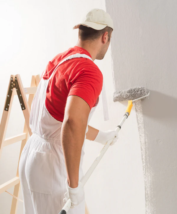 A professional painter from one of the top interior painting companies in Brentwood TN using a roller to apply light grey paint to a residential wall.