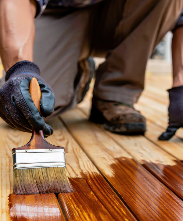 A close-up shot of a paintbrush applying a rich mahogany finish to wooden planks for a deck staining job in Brentwood, TN.