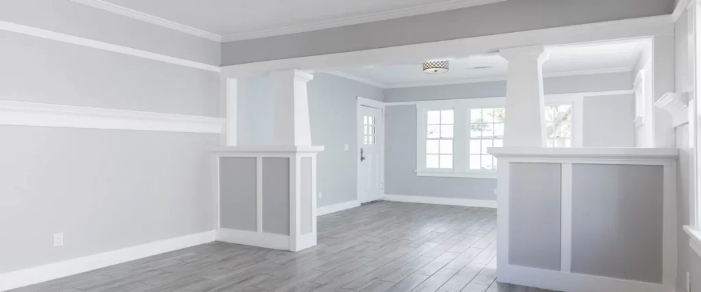 An empty spacious room with fresh light grey paint on the walls and decorative white wooden wainscoting and pillars.