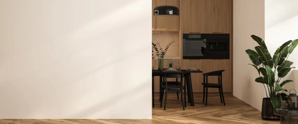 A contemporary open-concept dining area and kitchen featuring a large light beige partition wall, wooden cabinetry, and black dining furniture.