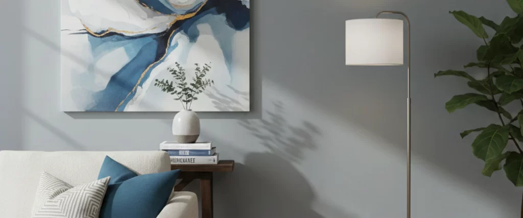 A close-up of a modern living room corner featuring a soft gray with blue undertones wall decorated with an abstract blue and gold painting and a white floor lamp.