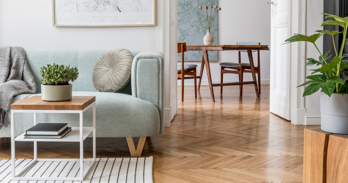 A bright, modern living room featuring professional house painting on white walls with a light blue sofa and herringbone wood floors.