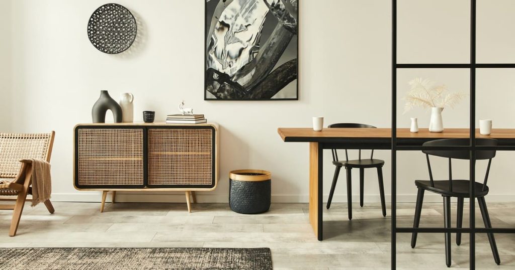 A bright minimalist dining area with a wooden table, woven sideboard, and off-white walls demonstrating neutral paint colors to brighten a room.