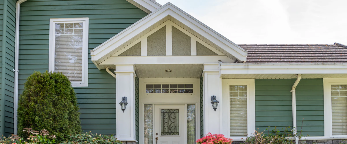 Close-up of a residential home exterior with high-quality green siding and white trim painting.