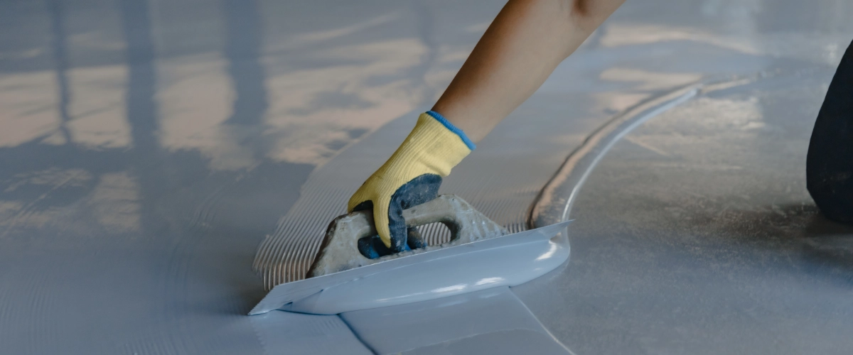 Worker using a trowel to spread and smooth a commercial floor coating during a painting or resurfacing project.