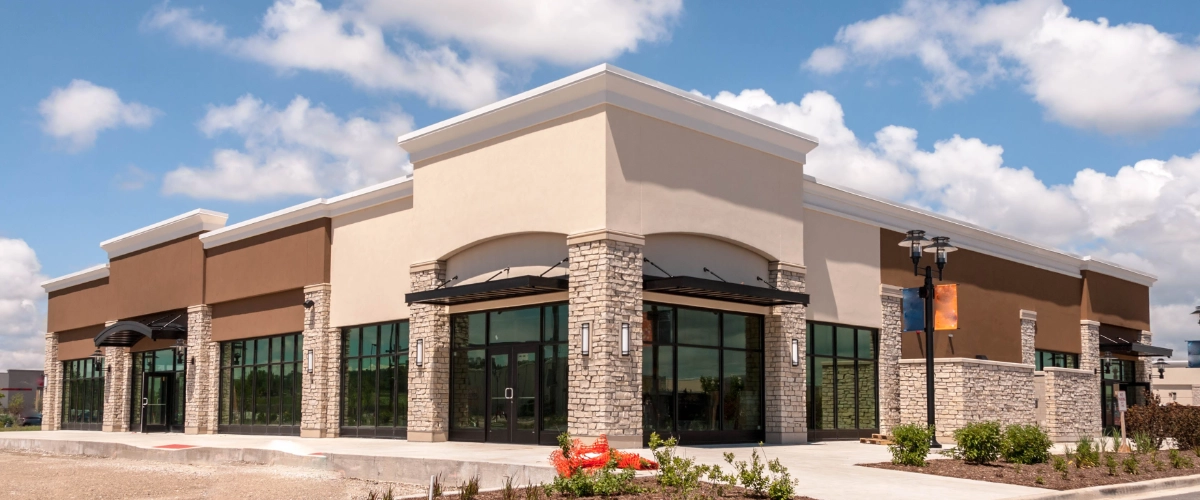 Newly painted commercial retail building with stone columns, large glass windows, and modern storefront exterior.
