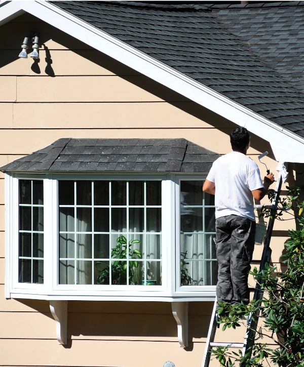 A man on a ladder working on home exterior painting